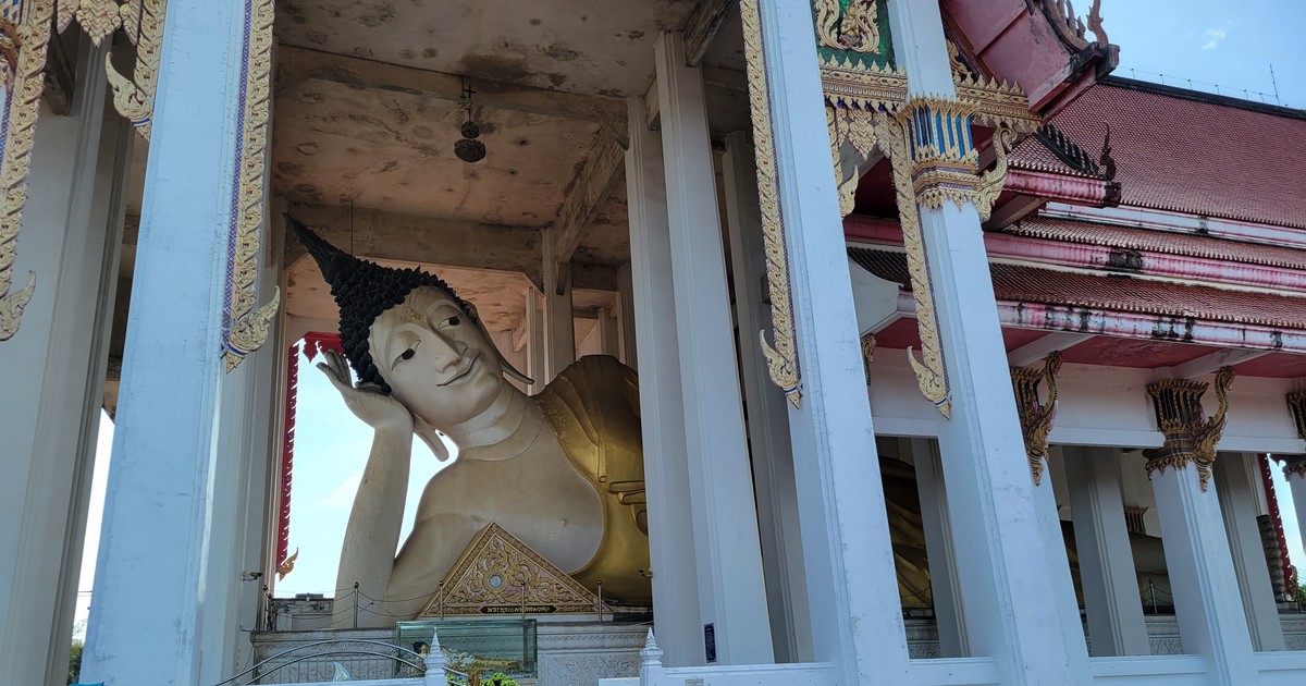 タイの寺院の大きな涅槃像（寝釈迦仏）。白い柱と朱色の屋根のお堂に横たわる金色の仏像